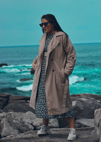 Young woman standing on rock at beach against sky