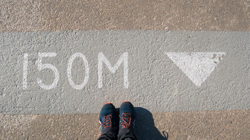 Low section of man wearing shoes standing by number on road