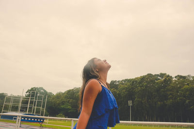 Side view of young woman standing at stadium against sky