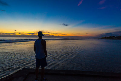 Rear view of man standing at beach during sunset