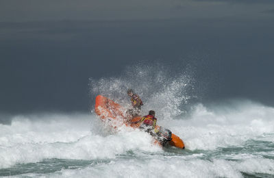 People in lifeboat on sea with splashing wave