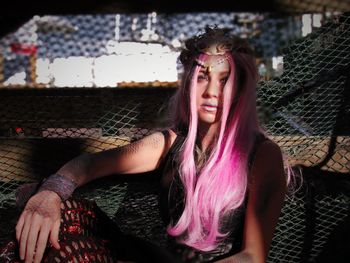 Portrait of woman with dyed long pink hair sitting against net