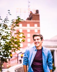 Portrait of smiling young man in city against sky