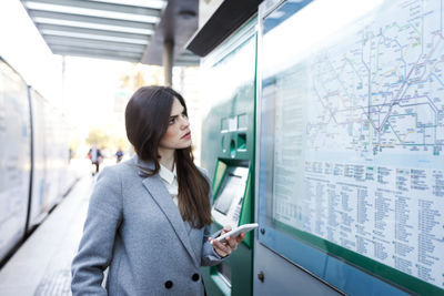 Spain, barcelona, young woman with smartphone looking at map at station