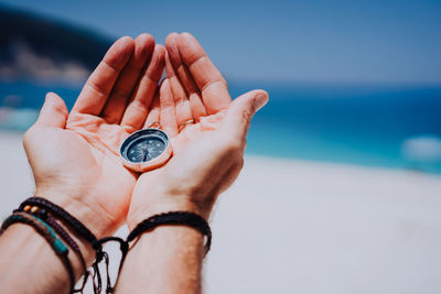 Cropped image of hands holding navigational compass at beach