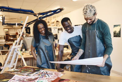 Happy men with woman looking at painting while standing at table in art class