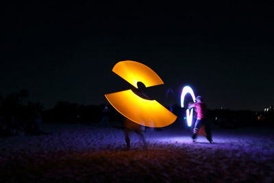 Rear view of man and woman walking on illuminated road at night