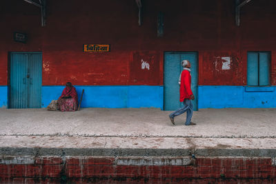 Rear view of man walking on footpath against building