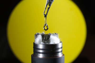 Macro shot of liquid drop on electronic cigarette against yellow background