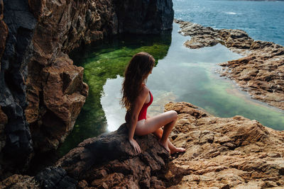 High angle view of woman sitting on rock over sea