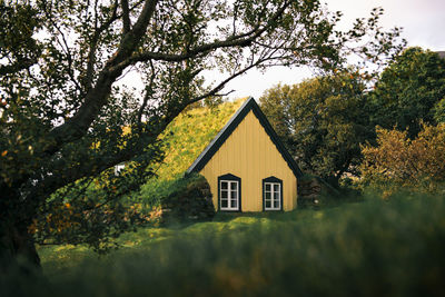 House and trees on field against sky