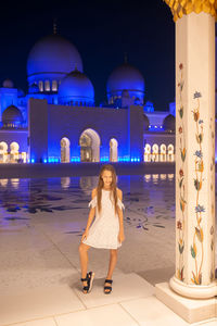 Full length portrait of woman standing against illuminated building