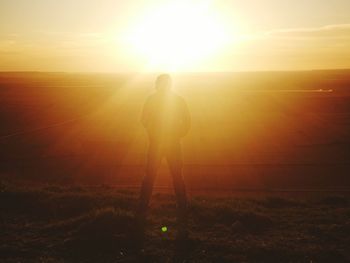 Rear view of silhouette man standing on mountain against bright sun during sunset