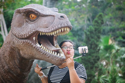 Woman puckering while taking selfie with dinosaur statue in park