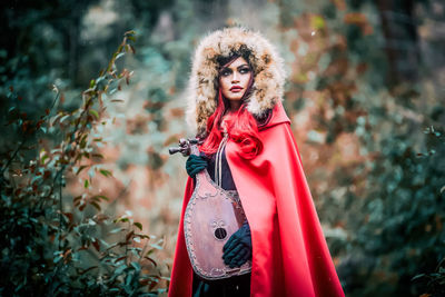 Woman in costume holding string instrument while standing in forest