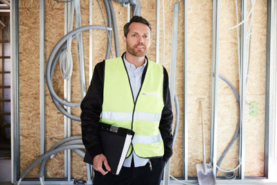 Mature architect with file standing at construction site on sunny day
