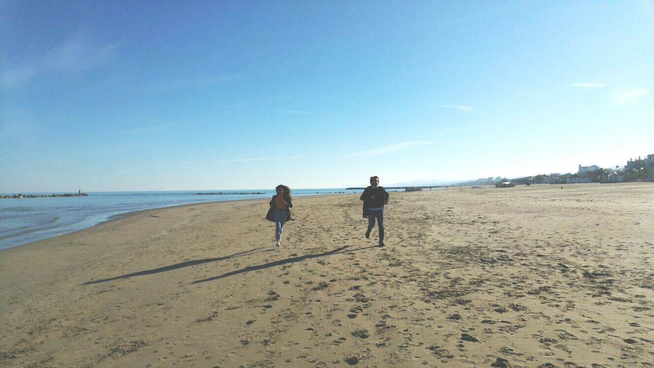 REAR VIEW OF MEN WALKING ON BEACH