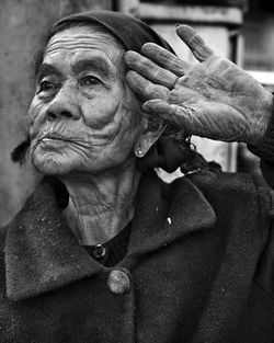 Close-up of senior woman saluting while standing against wall