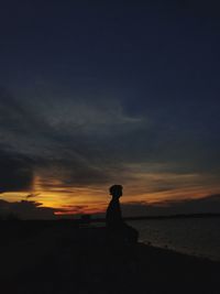 Silhouette man sitting on beach against sky during sunset