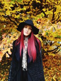 Portrait of young woman standing against trees during autumn
