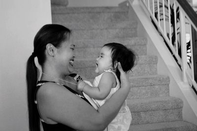 Cheerful mother with daughter standing by steps at home