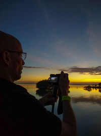 Portrait of man photographing against sky during sunset