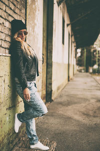 Fashionable young woman wearing jacket standing against brick wall