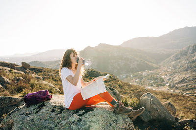 Woman sitting on rock against sky