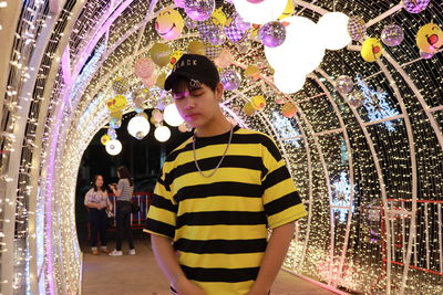 Full length of young man standing against illuminated lights at night
