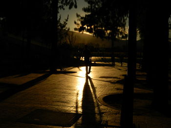 Silhouette people walking on footpath by street against sky during sunset