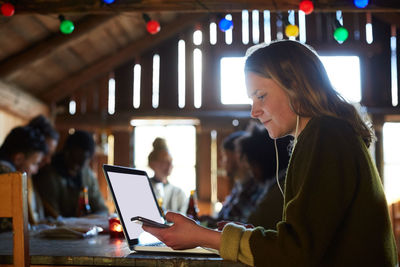 Young woman using laptop on table while friends talking in background at home