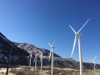 Low angle view of windmills against clear blue sky