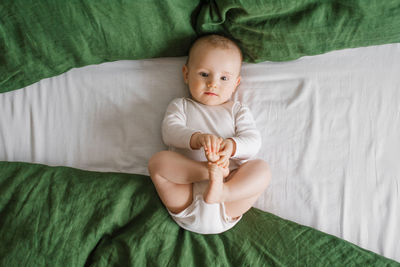 Top view of a charming smiling caucasian 6-month-old boy dressed in a bodysuit, holding his legs 