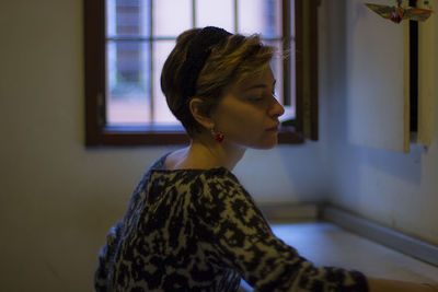 Side view of young woman against window