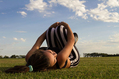 Woman lying on grass against sky