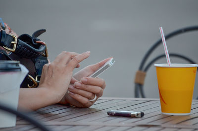 Cropped hands of woman using phone at table