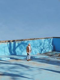 Rear view of man standing at swimming pool against sky