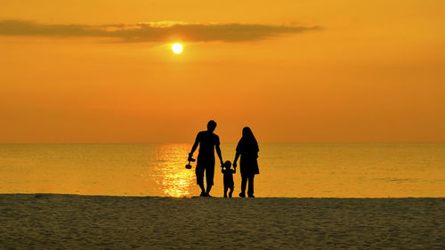 Silhouette family walking at beach against sky during sunset