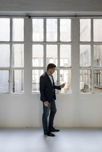 Businessman standing in a loft at the window using cell phone