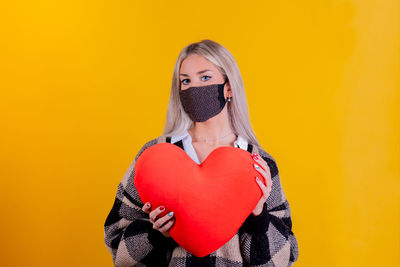 Portrait of woman with heart shape against yellow background