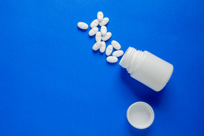 Directly above shot of pills spilling from bottle against blue background