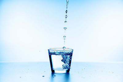 Close-up of drop falling on glass against blue background