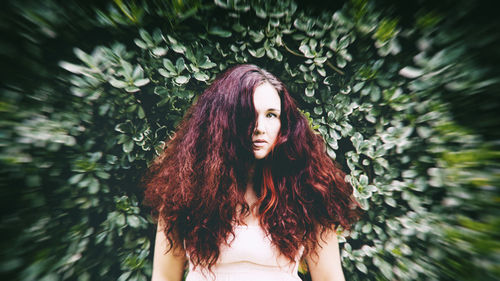 Front view of woman red hair in front of green leaves staring at camera