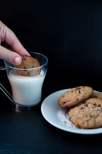 Close-up of hand holding chocolate cookie on glass of milk