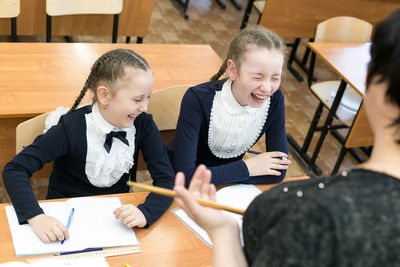 High angle view of teacher with happy students laughing while sitting on table