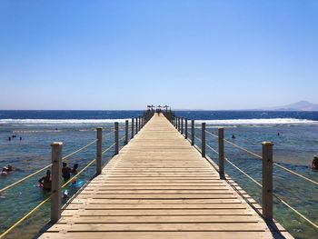 Pier over sea against clear blue sky