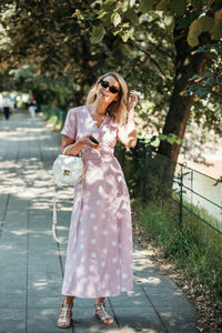 Portrait of happy young woman wearing sunglasses standing on footpath