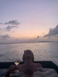 Man relaxing by swimming pool against sky during sunset