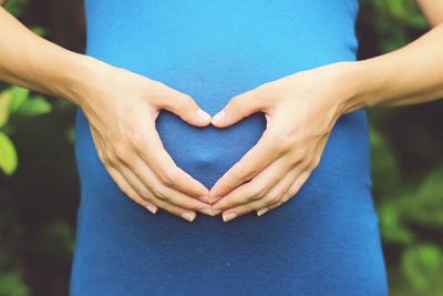 Midsection of pregnant woman making heart shape on abdomen