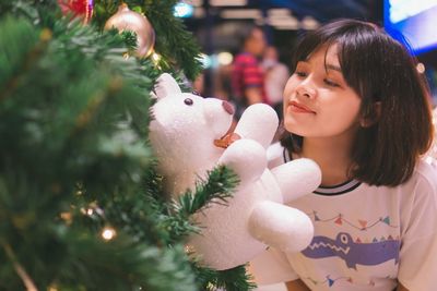 Young woman looking at stuffed toy hanging from christmas tree